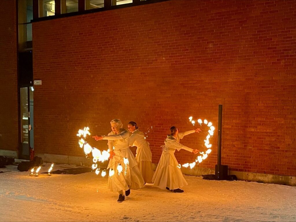 En eldshow där flera personer iklädd vita klänningar håller i snören som brinner och vevar runt dessa i luften.